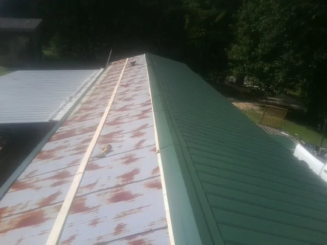 Old rusted panels beside newly installed green metal roofing — Wind Damage Roof Repair by Roofing Brothers in Ionia